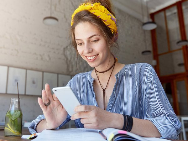 A woman wearing a yellow bandana looking at her phone and smiling