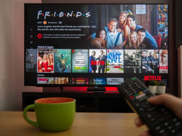 First-person photo of someone using remote control to scroll through Netflix menu on TV