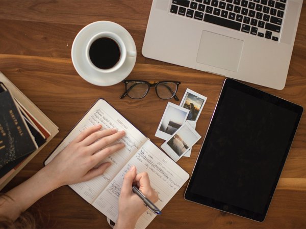 A person writing on a notepad at a wooden table