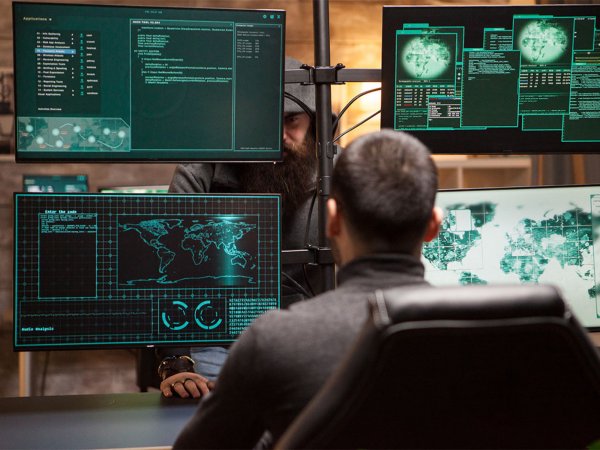 Two men sit in front of computers and code