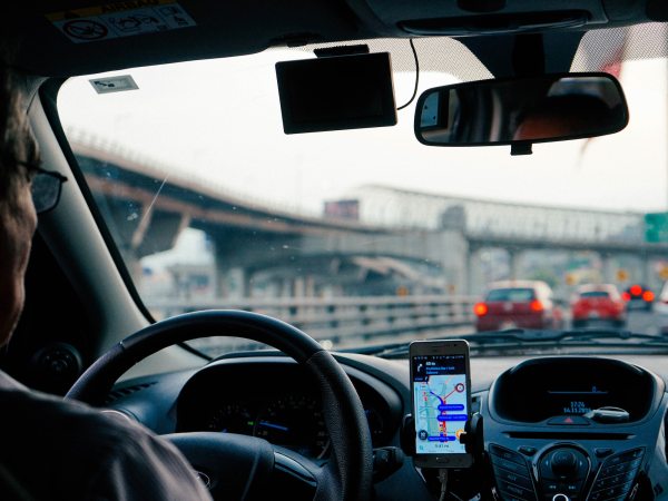 Interior rear passenger view of man driving car with Uber app on phone attached to dashboard.