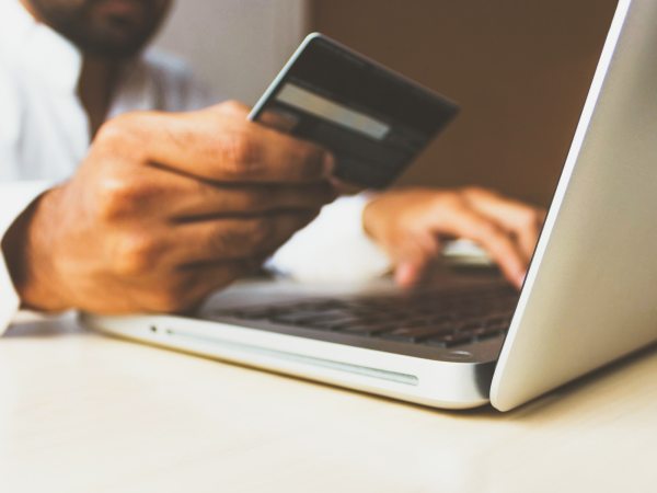 Stock image of person holding debit card next to laptop for financial transaction