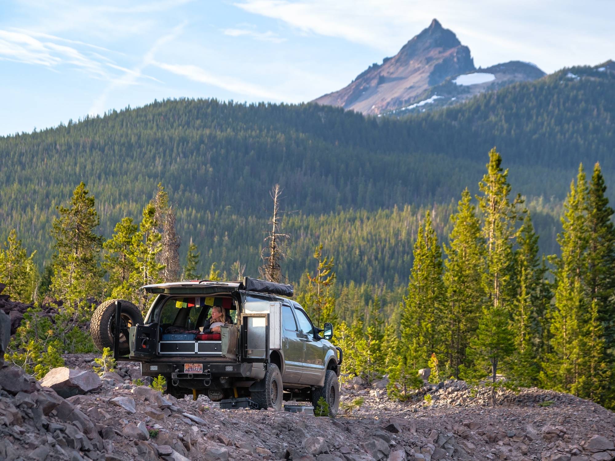 vehicle with open back doors overlanding outdoors with person laying on the back of the vehicle