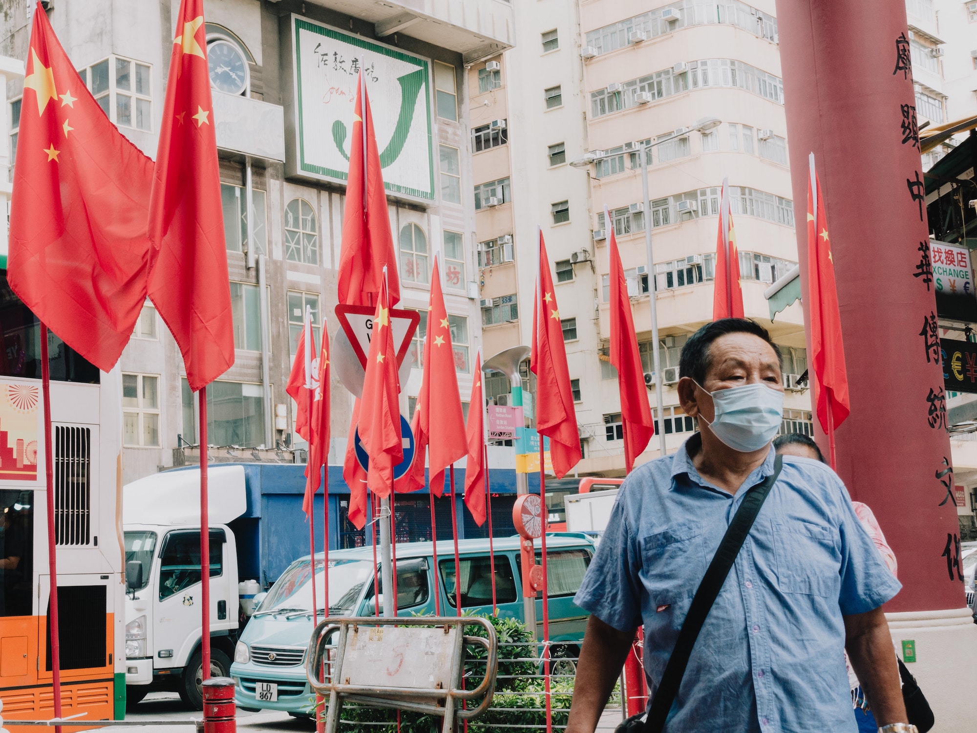Chinese man wearing COVID-19 mask walking down city street in China with national flags behind him