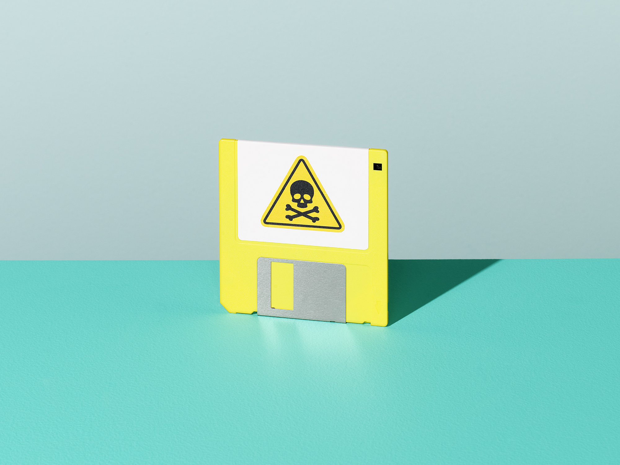 A yellow floppy disk with a poison symbol on it, standing upright on a teal surface.