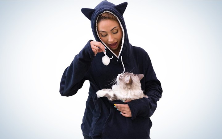  A woman wearing a navy blue cat hoodie with a cat in the pouch.