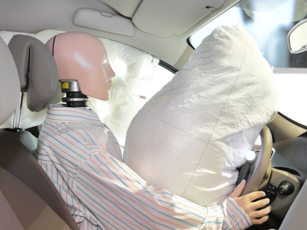 Crash test dummy in driver's seat of car with airbag deployed