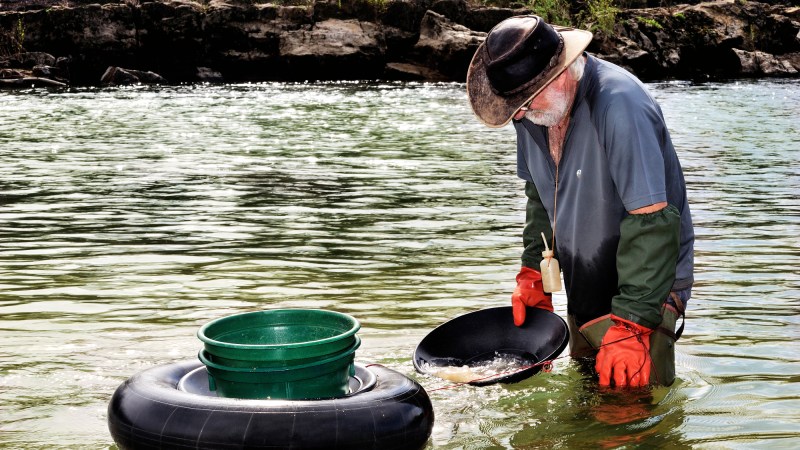 An old man panning for gold in a river.