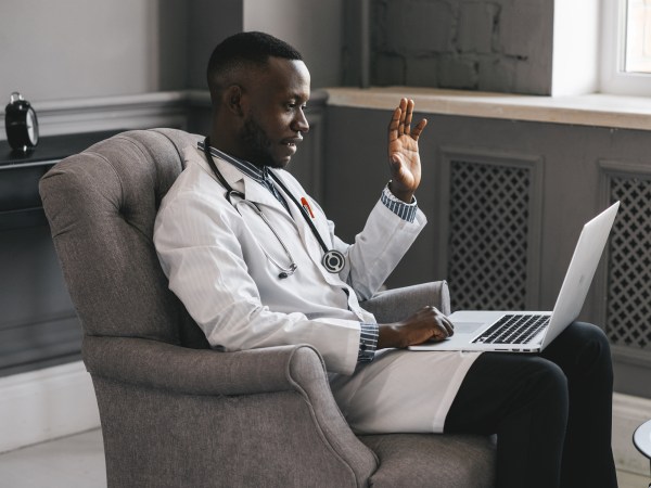 Doctor sitting in chair and waving at laptop camera for telehealth session