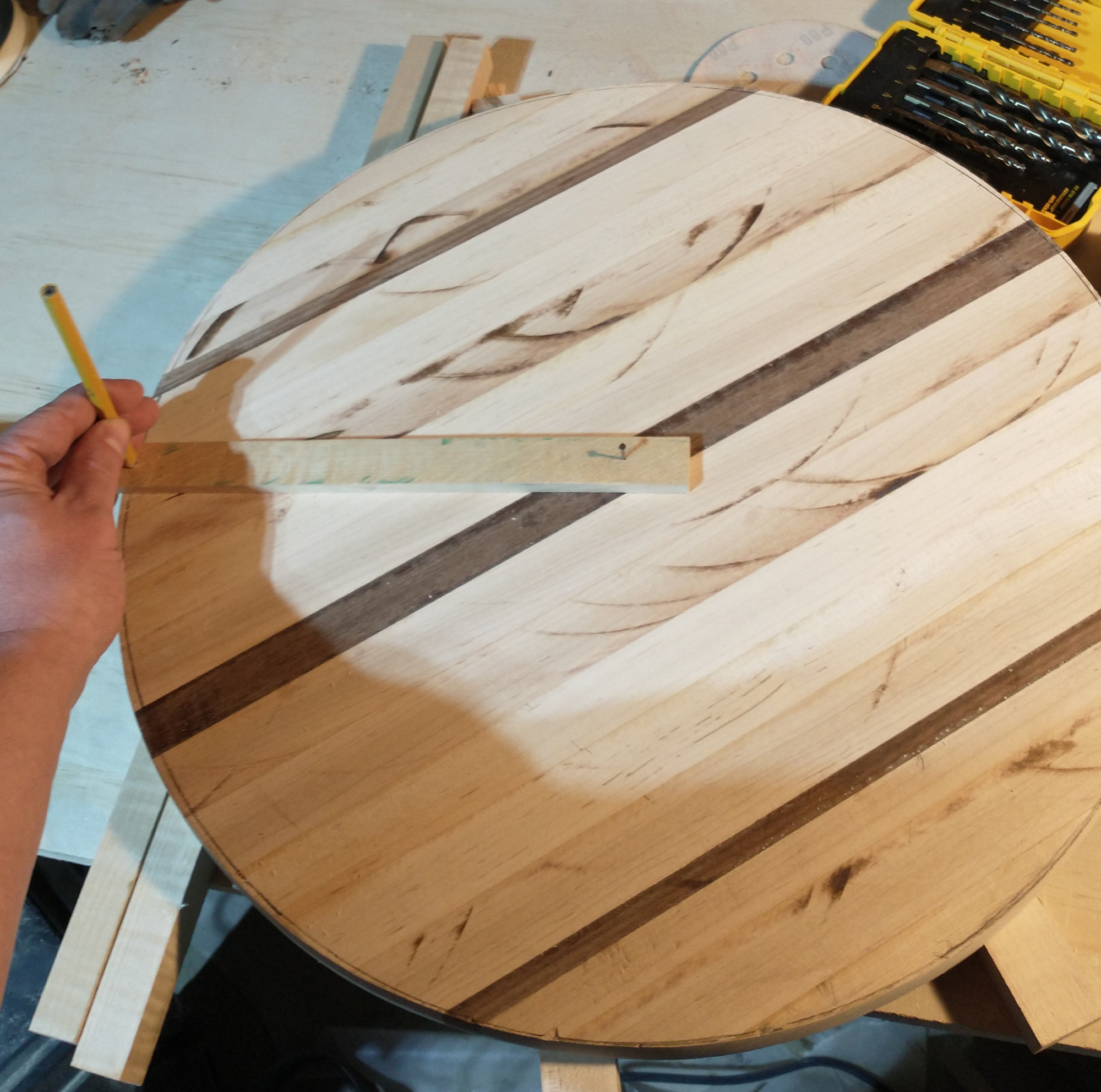 A tip for tracing a circle on wood: a nail in the center of a roughly circular board, holding a piece of wood in place, with a pencil in the other end, so it can be rotated around the central point.