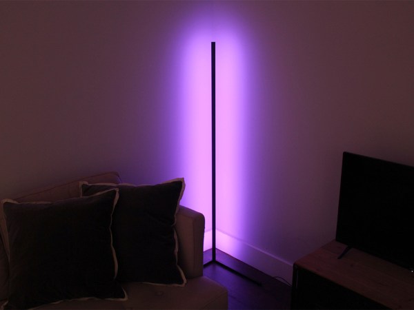 A color changing corner lamp set to purple leans against a wall in the living room