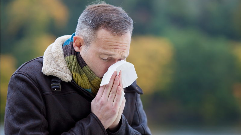 A man wearing a jacket sneezes into a rissue.