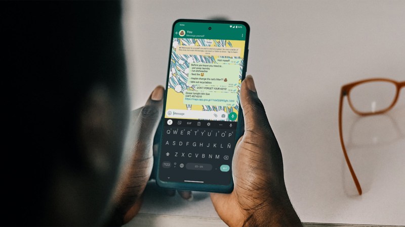 person sitting at desk looking at phone with whatsapp open messaging themselves