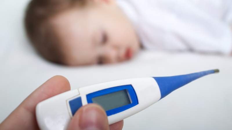 A sleeping baby with an adult holding a thermometer.