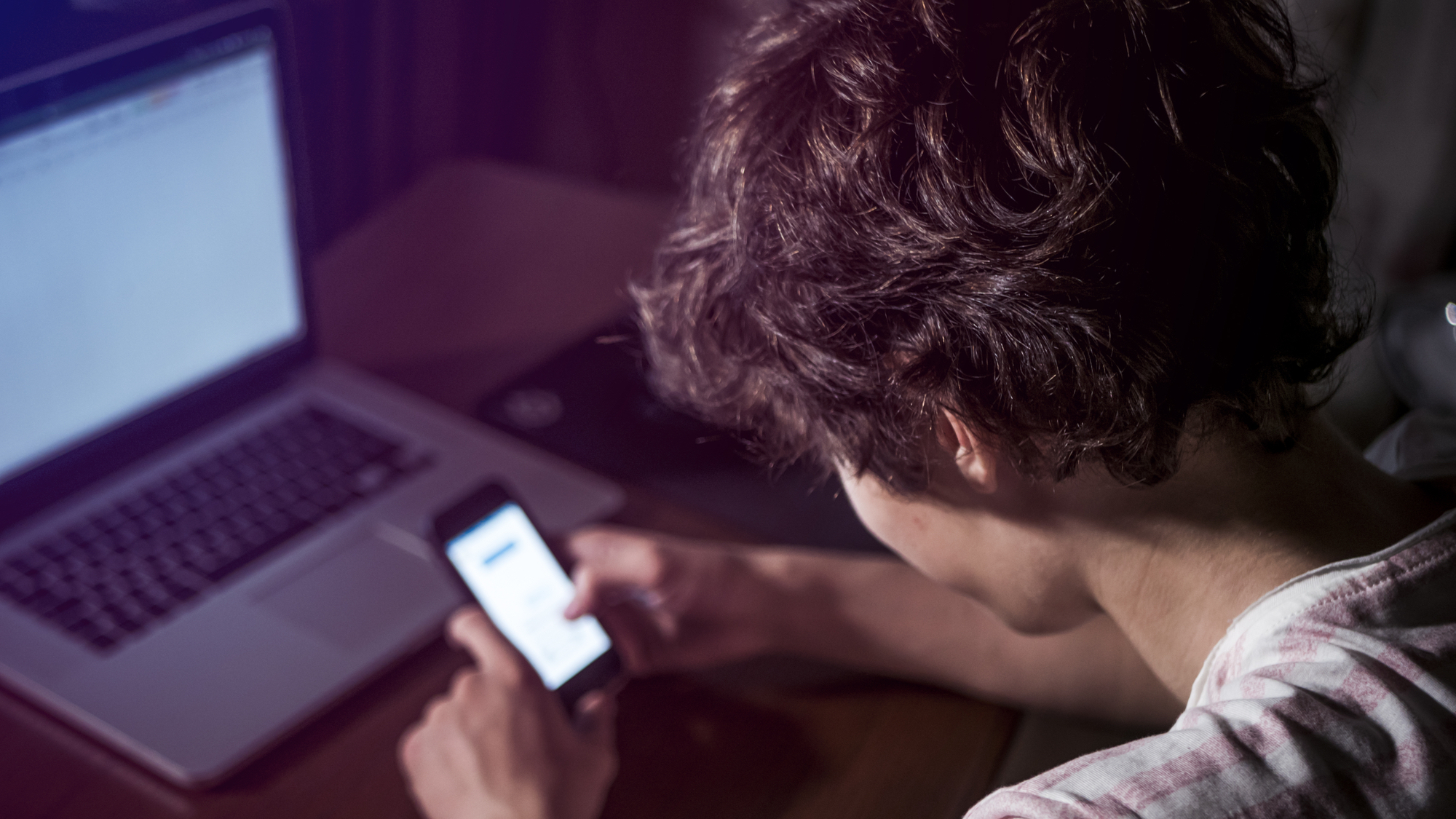 overhead angle of teen using smartphone in front of laptop on table