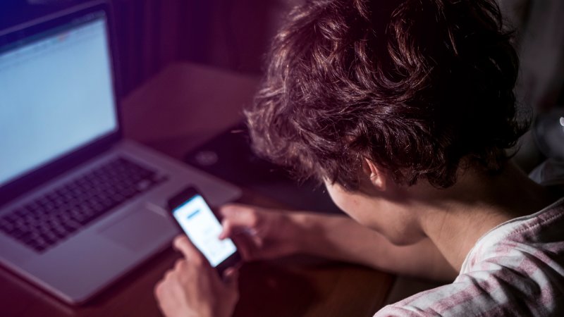 overhead angle of teen using smartphone in front of laptop on table