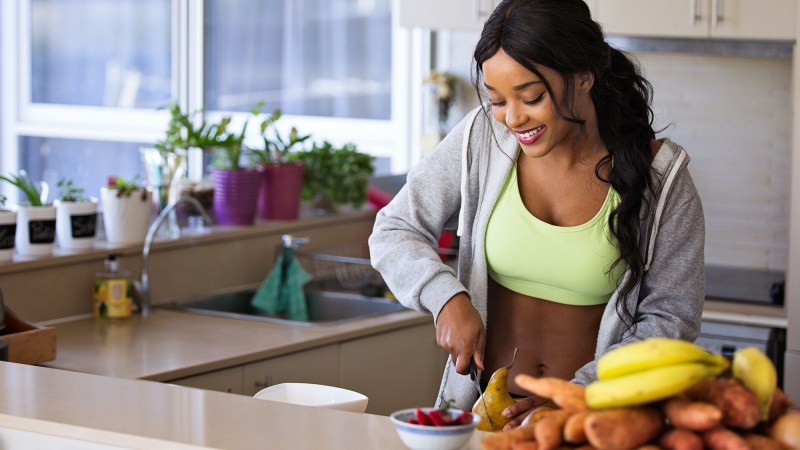 person-in-work-out-gear-standing-in-kitchen-chopping-fruit-