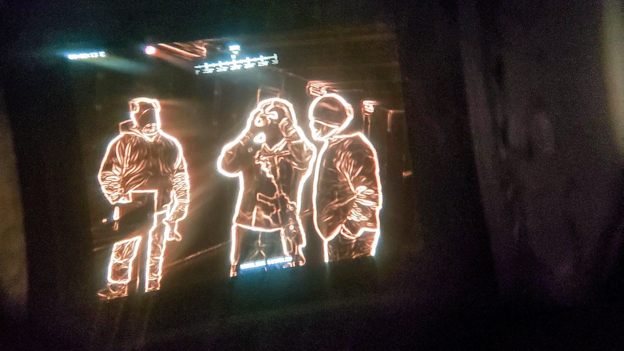 Three soldiers standing in a row, with the center one holding night vision goggles up to his eyes, viewed through night vision and thermal sensing.