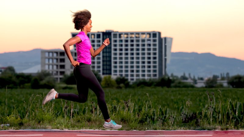 a young black woman jogging outside on a track smiling