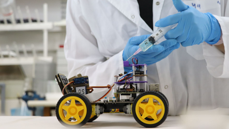 Scientist holding syringe next to wheeled robot with biological sensor