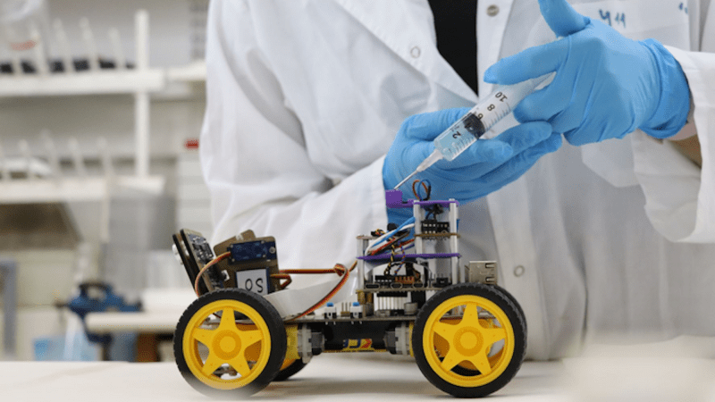 Scientist holding syringe next to wheeled robot with biological sensor