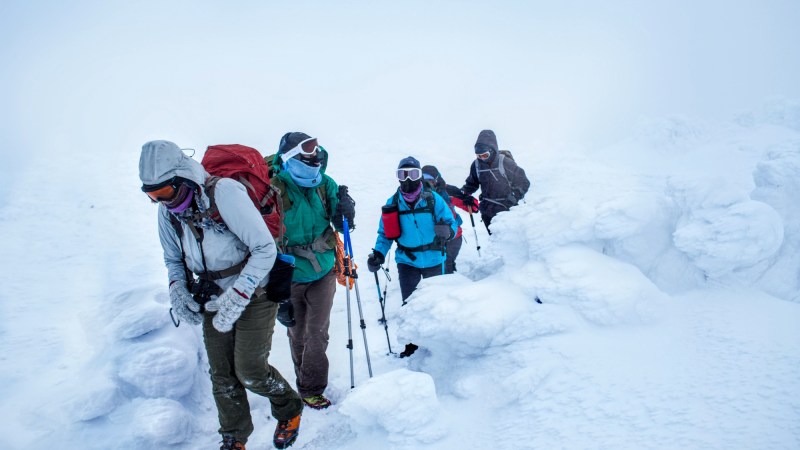 Four people hiking through a snowy landscape, all very bundled up to prevent frostbite.