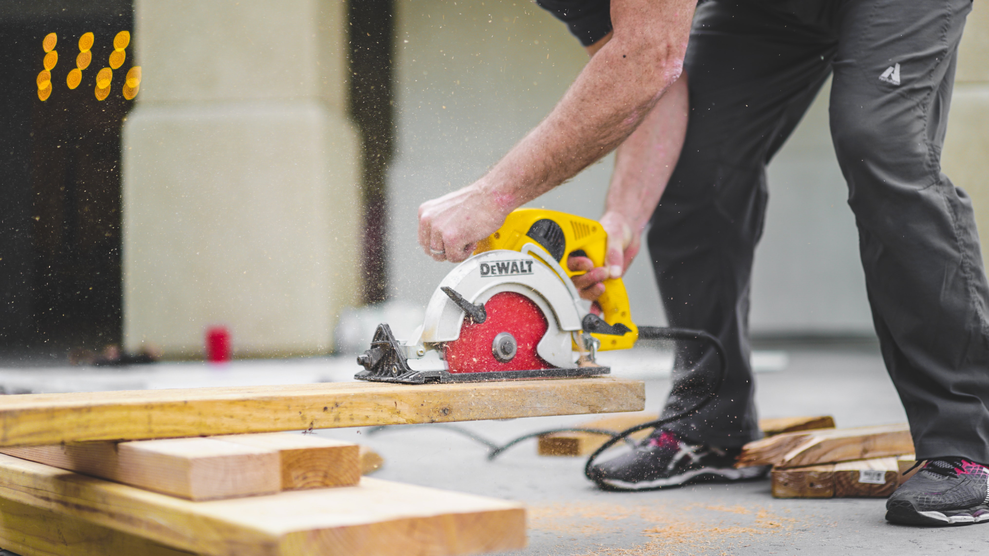 A person standing over a board, using a circular saw to rip it to width, hopefully considering woodworking safety.