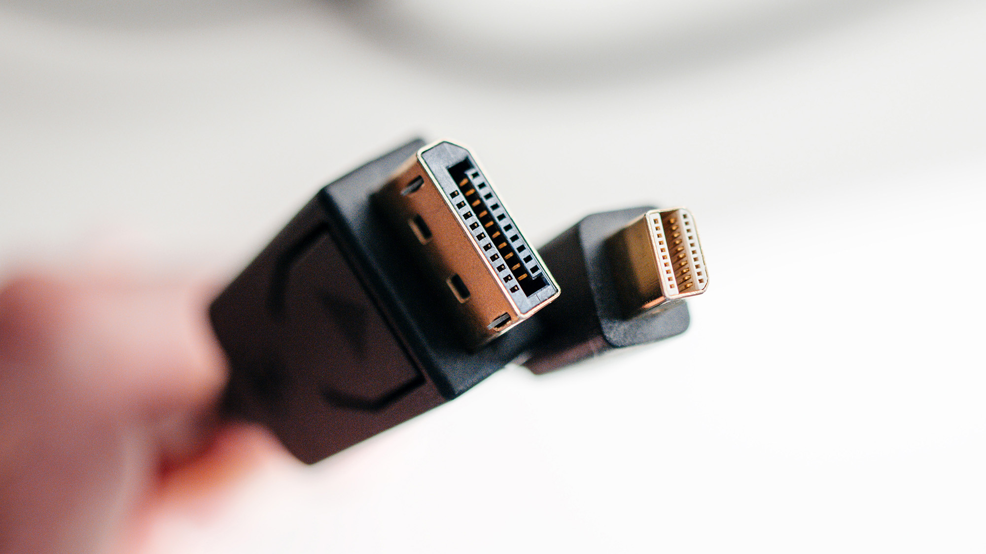 close up of a hand holding a regular DisplayPort and a mini DisplayPort cables