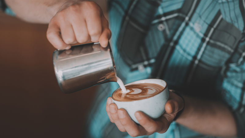 A male barista pours milk into coffee.