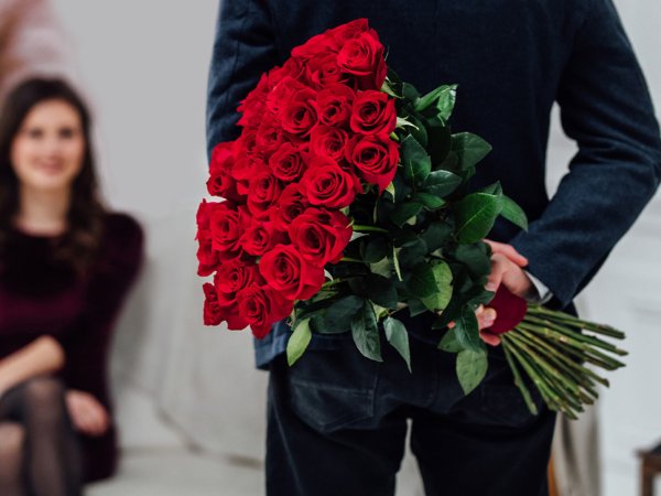 A person surprising their partner with a bouquet of roses for Valentine's Day.