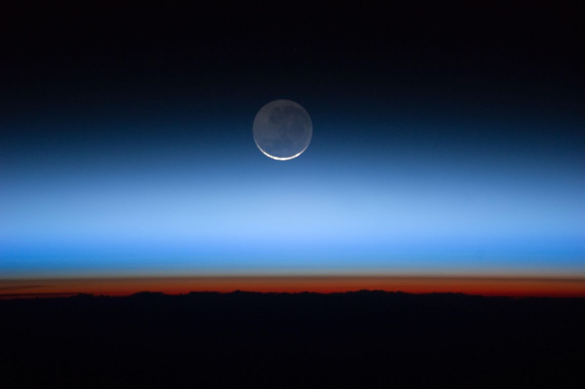 The Earth's atmosphere from the ISS, with the moon in the background, showing clearly defined layers between the planet and space, where the Karman line separates the two.