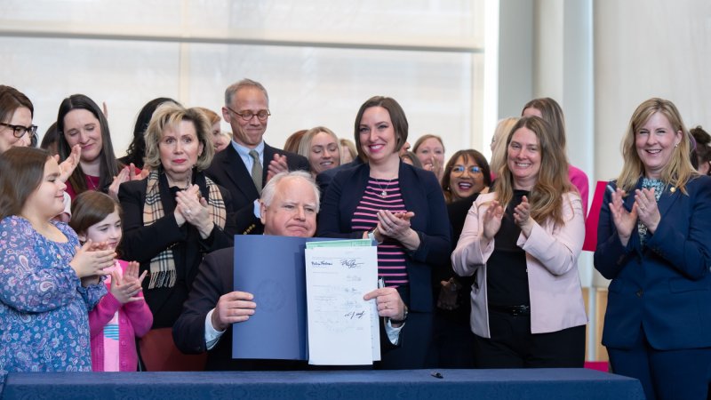 Minnesota Governor Tim Walz holds up a piece of legislation, surrounded by supporters of the PRO Act.