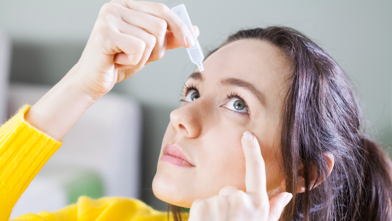 A young woman applies eye drops.