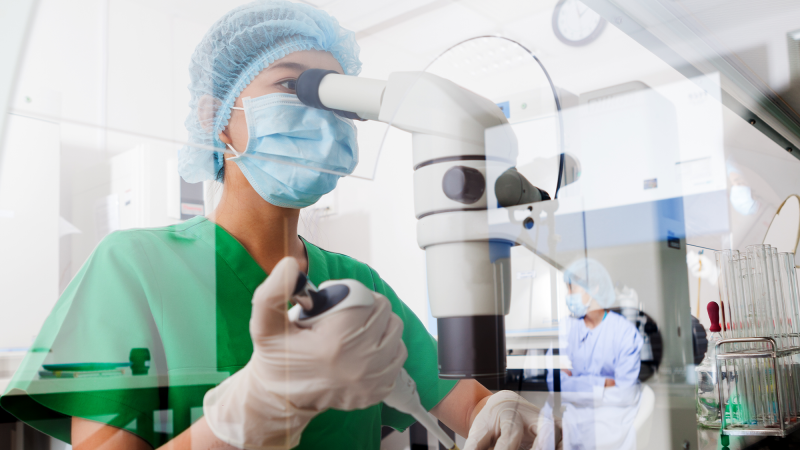 A scientist working at a microscope with a pipette.