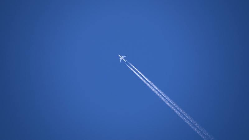A plane flying high above the ground, drawing white contrails across a blue sky.