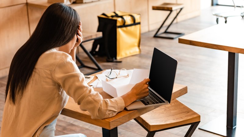 Woman hold head in hand while sitting at desk in front of laptop