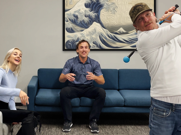 A person practices their golf swing in their living room with two friends.