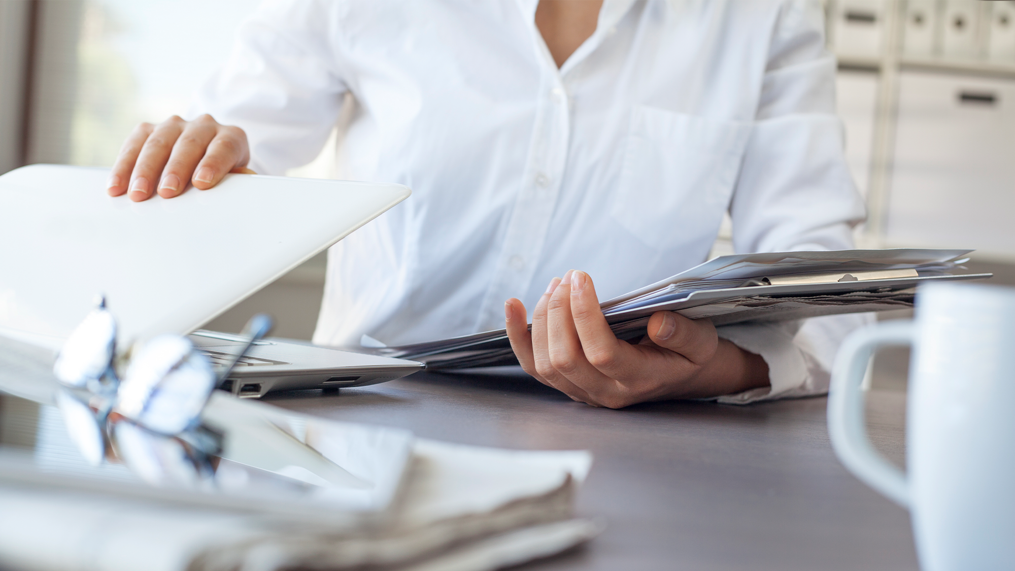 A business woman packs up paperwork and a laptop in an office.