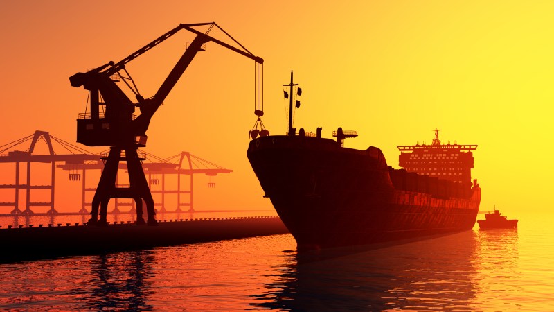 Crane loading cargo onto ship at sunset