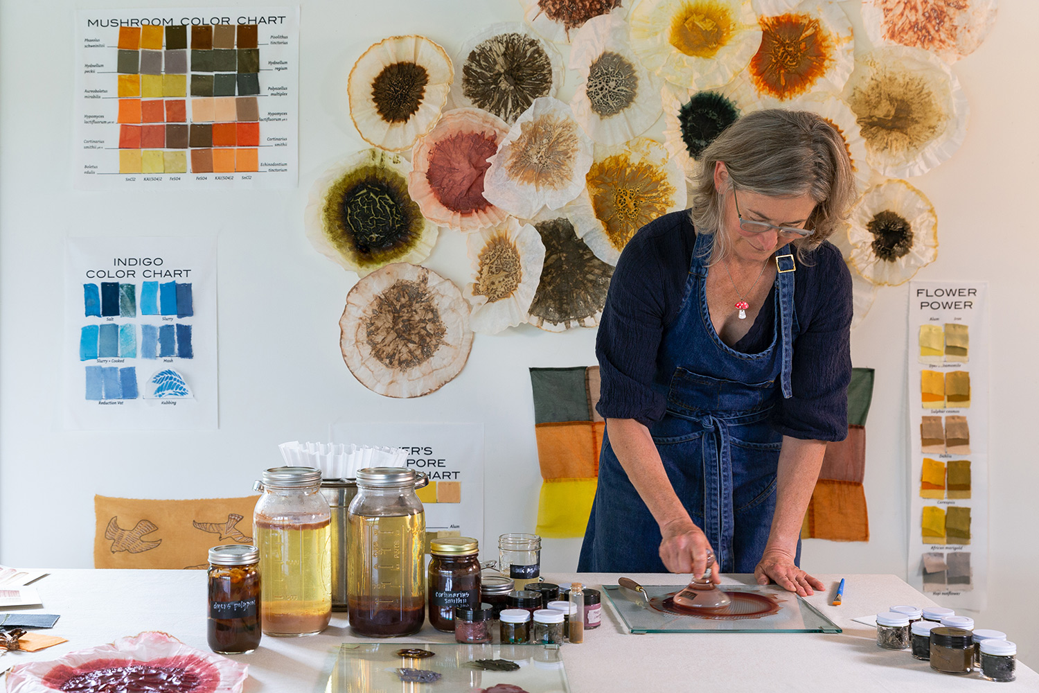 Woman with gray hair and a blue shirt in front of a wall with samples of mushroom paints