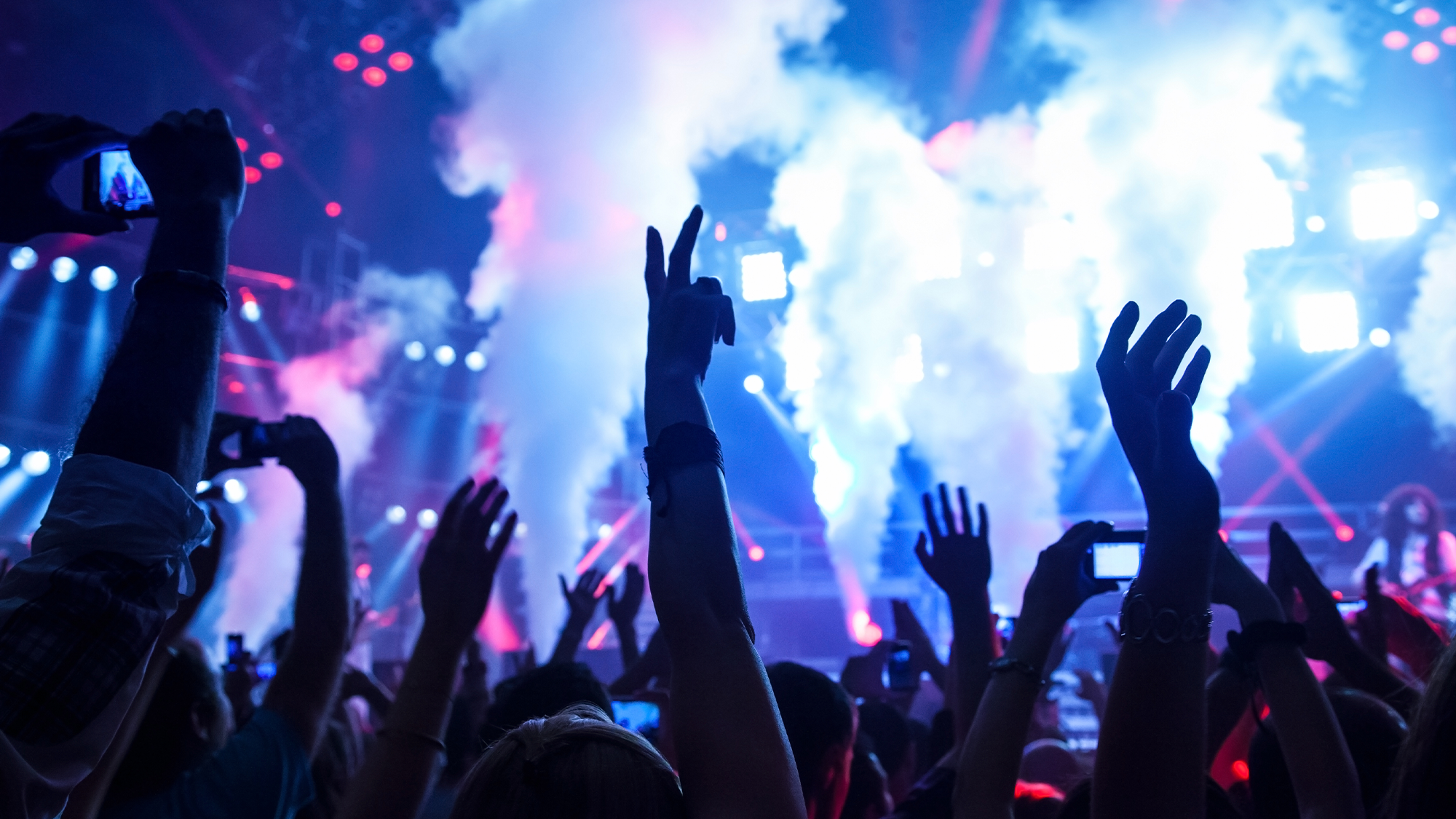 Attendees at a concert dance and one man records the performance on a smartphone.