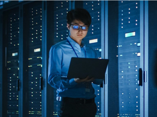 A person looks at a laptop in front of a row of computers.