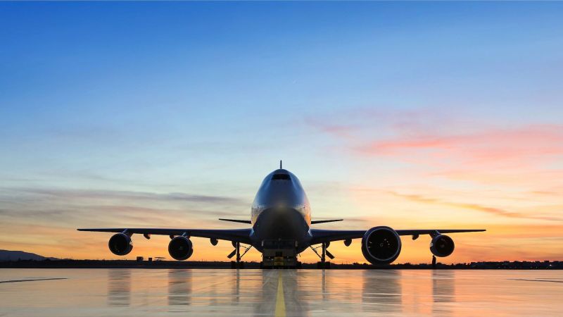 A 747-400 outside at sunset, with a GE9X engine on its left wing for testing.