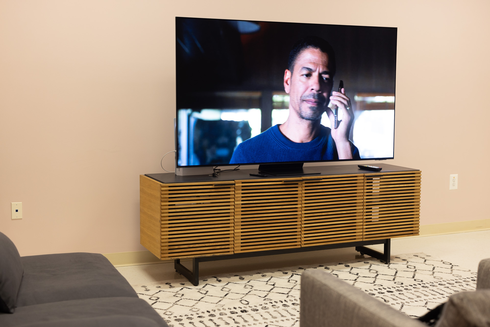 The Samsung S95C OLED TV on a stand in a room with pink-ish walls