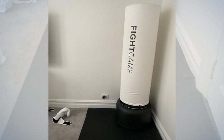  white fight camp boxing bag on a black mat with white boxing gloves next to it