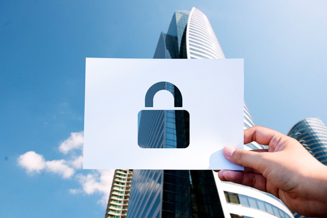 A person holding a printed cut out of a padlock in front of a city building