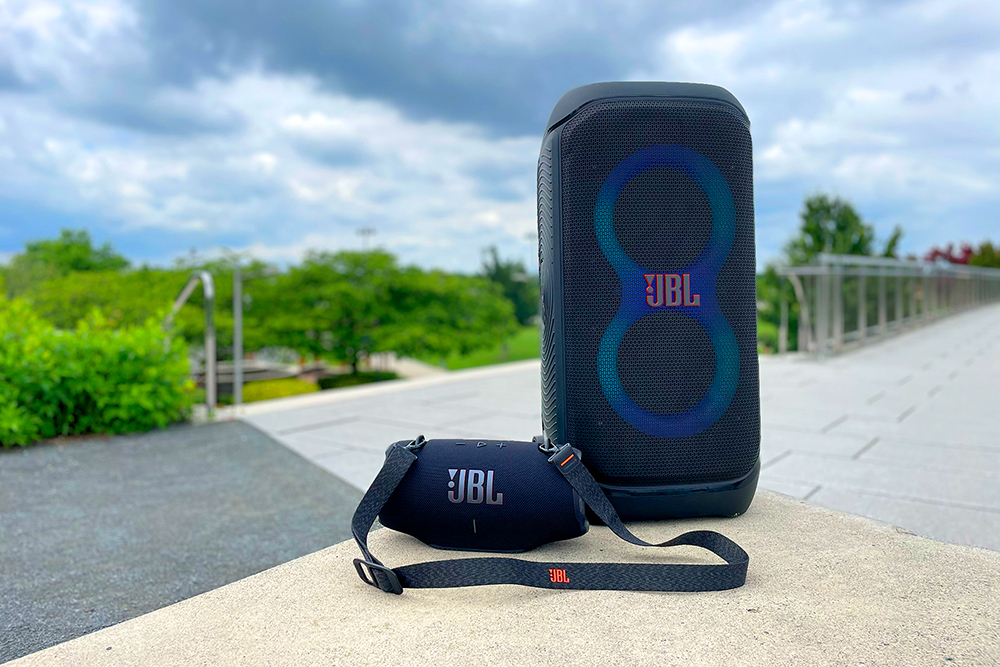 Black JBL PartyBox 320 and Xtreme 4 party speakers sitting on a concrete bench.