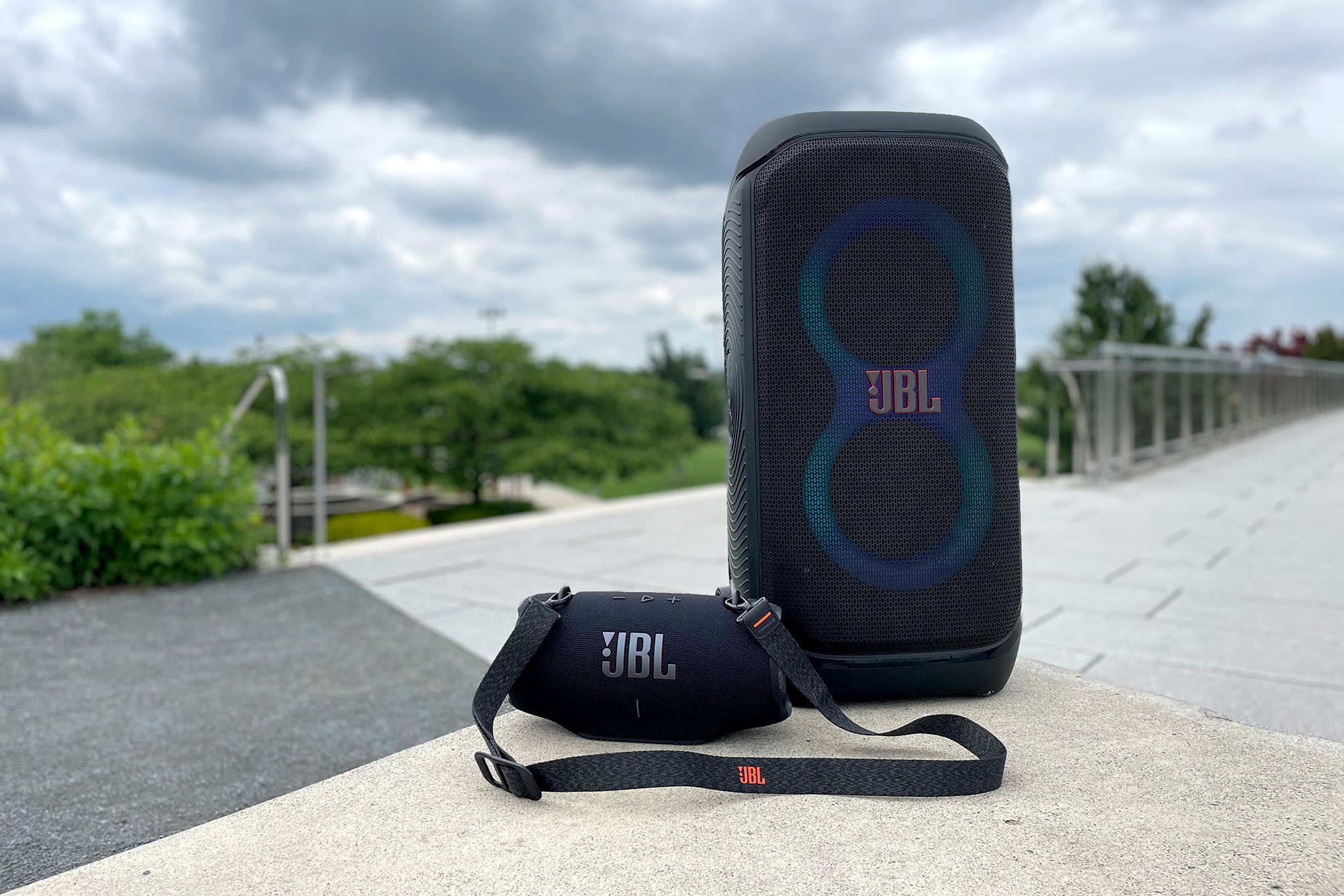 Black JBL PartyBox 320 and Xtreme 4 party speakers sitting on a concrete bench.