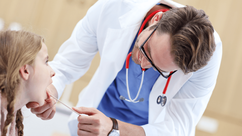 A doctor examines a child's throat with a tongue depresser.