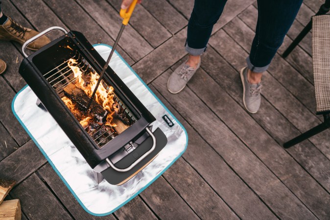 Biolite FirePit+ with a fire in it and someone is poking the fire with a stick.